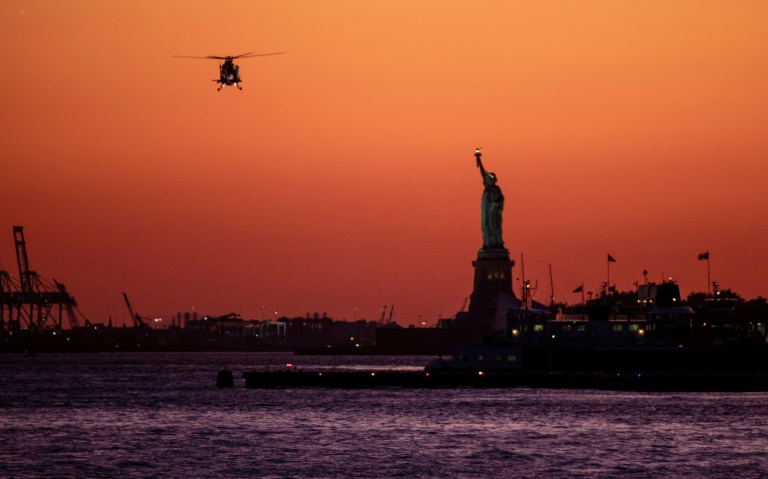 In this file photo taken on October 14, 2019 a helicopter flies past the Statue of Liberty as the sun sets in New York City