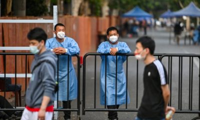 Workers wearing protective gear stand behind a fence blocking a street in a residential area under a Covid-19 lockdown in the Huangpu district of Shanghai