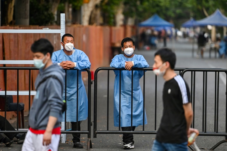 Workers wearing protective gear stand behind a fence blocking a street in a residential area under a Covid-19 lockdown in the Huangpu district of Shanghai