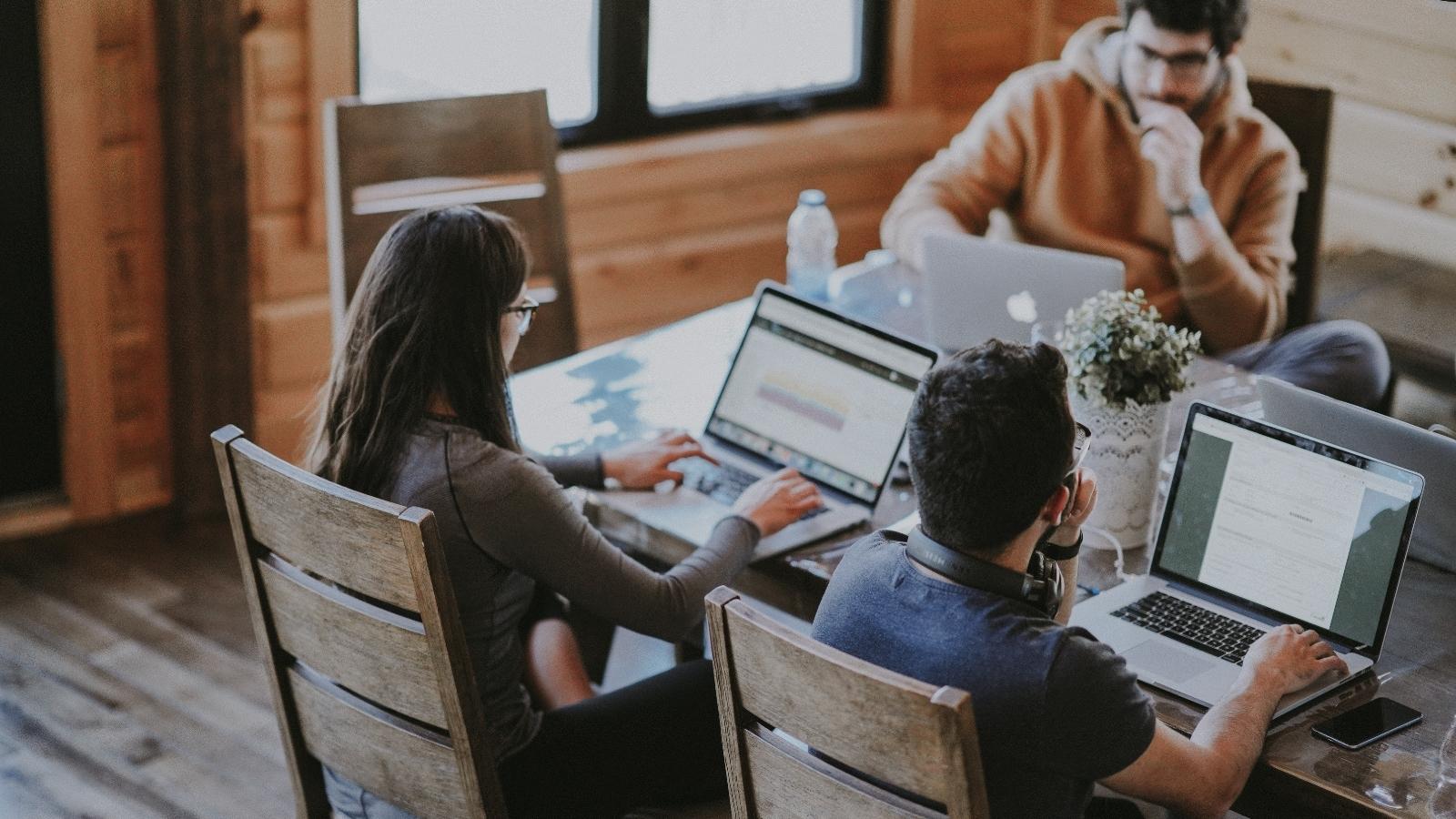 Three people using Macbooks at a table