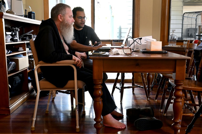 Rodney Gorham, who has a Synchron brain implant, works on a computer at his home in Melbourne with clinical field engineer Zafar Faraz